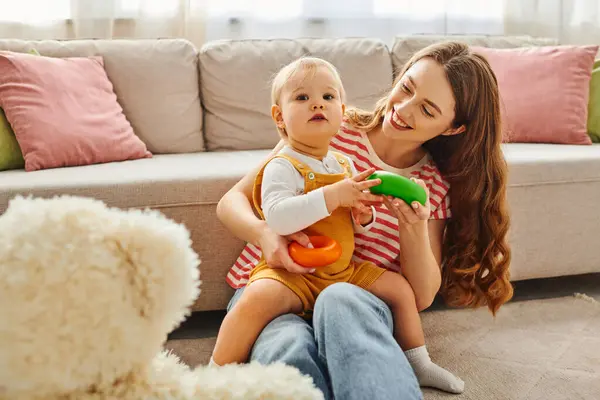 A young mother sitting on the floor, tenderly holding her baby daughter in a loving embrace. — Stock Photo