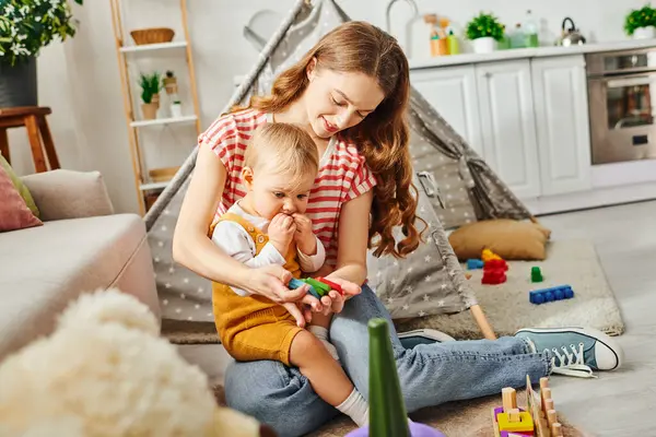 A young mother joyfully interacting with her toddler daughter in a cozy living room setting, fostering a bond of love and laughter. — Stock Photo