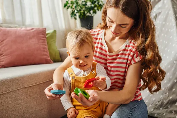 Une jeune mère interagit joyeusement avec sa fille en bas âge, s'engageant dans des activités ludiques sur le sol à la maison. — Photo de stock