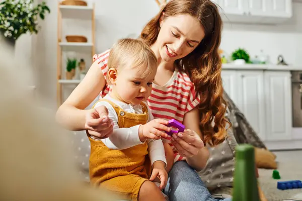 A young mother and her toddler daughter engrossed in game, sharing a moment of technology-driven playtime at home. — Stock Photo