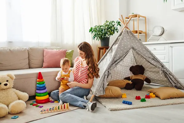 Une jeune mère assise sur le sol avec sa petite fille, partageant un moment spécial d'amour et de proximité à la maison. — Photo de stock