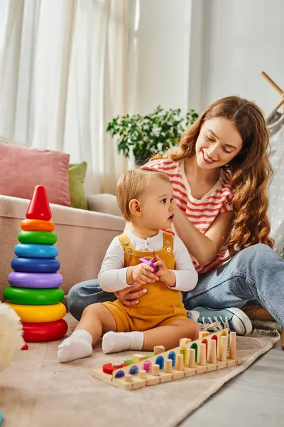 Eine junge Mutter beschäftigt sich freudig mit ihrer kleinen Tochter auf dem Fußboden und fördert durch das Spielen eine starke Bindung. — Stockfoto