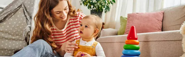 A young mother happily engages with her toddler daughter, both sitting on the floor, laughing and playing together. — Stock Photo