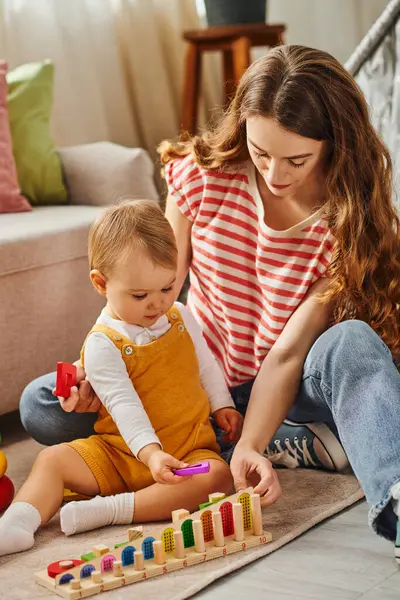 Una giovane donna gioca felicemente con sua figlia sul pavimento della loro casa. — Foto stock