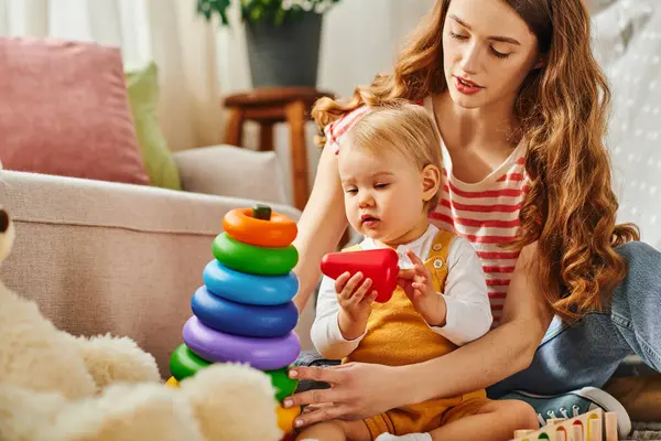 Una joven mujer jugando alegremente con su hija pequeña en el suelo en casa, creando recuerdos duraderos de felicidad. - foto de stock