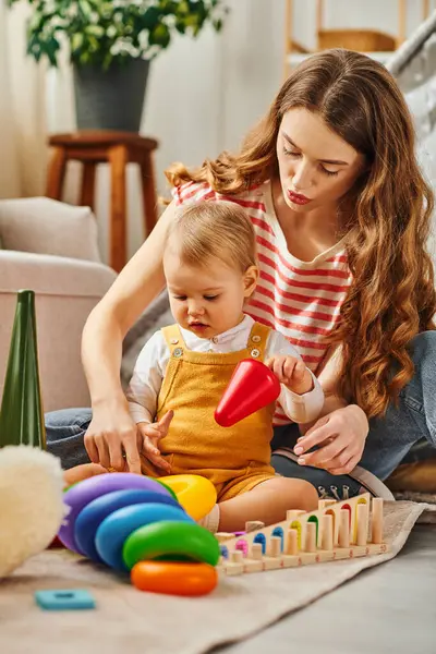 Молода мати радісно взаємодіє зі своєю дочкою малюка, коли вони грають разом на підлозі вдома. — стокове фото