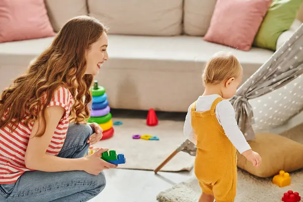 A young mother joyfully engages with her toddler daughter in cheerful play in a cozy living room setting. — Stock Photo
