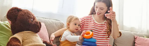 A young mother and her toddler daughter joyfully engage in playful interactions on a cozy couch at home. — Stock Photo