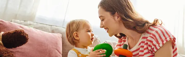 A young mother playing with her toddler daughter on a cozy couch, sharing moments of joy and connection. — Stock Photo
