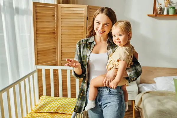 Happy young mother lovingly cradles her toddler daughter in her arms, creating a tender moment of connection and affection at home. — Stock Photo
