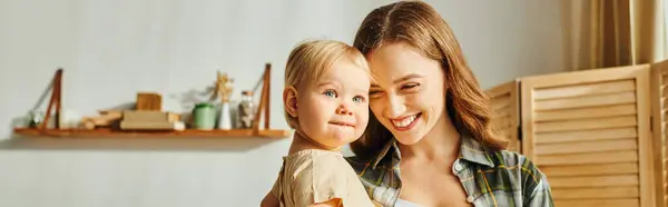 Une jeune mère tient tendrement sa petite fille dans ses bras, partageant un précieux moment d'amour et de connexion à la maison. — Photo de stock
