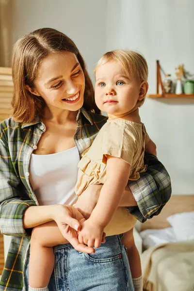 Молода мати ковтає доньку малюка на руках, ділячись миттю любові та зв'язку вдома. — стокове фото