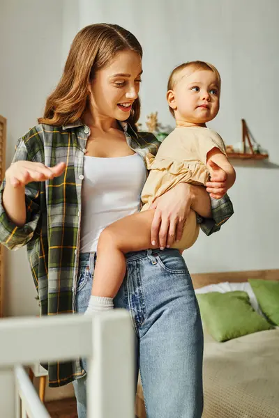 A young mother lovingly holds her toddler daughter in her arms, sharing a moment of bonding and affection at home. — Stock Photo