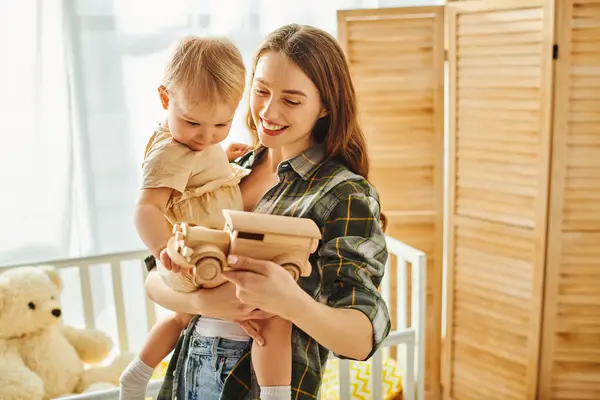 A young mother tenderly holds her toddler daughter in her arms, expressing love and affection in a cozy home setting. — Stock Photo