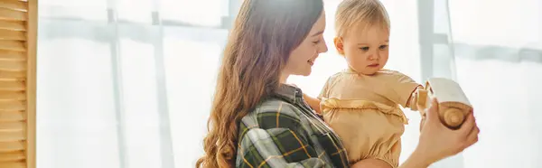 A young mother lovingly holds her toddler daughter in her arms at home, showing affection and care. — Stock Photo