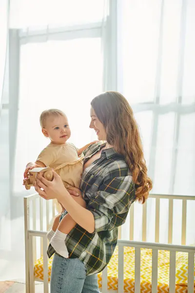 Une jeune mère berce amoureusement sa petite fille dans ses bras, partageant un doux moment de connexion et d'amour à la maison. — Photo de stock