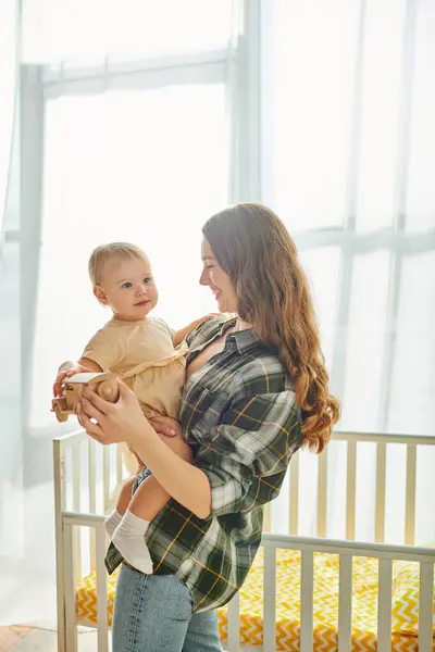 Una joven madre acuna amorosamente a su hija en brazos, compartiendo un dulce momento de conexión y amor en casa. - foto de stock