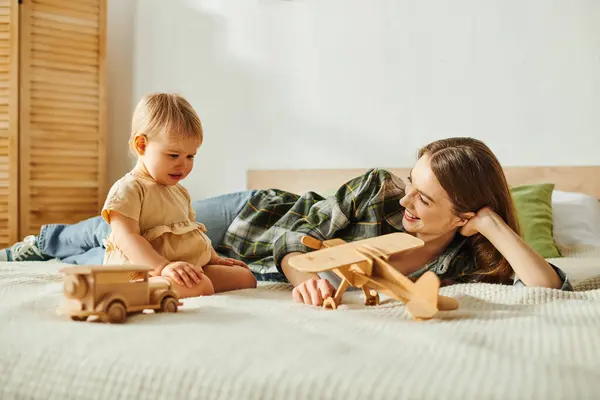Eine junge Mutter liegt auf einem Bett neben ihrer kleinen Tochter und teilt einen heiteren und herzerwärmenden Moment der Verbundenheit. — Stockfoto