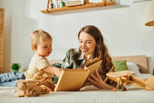 Una madre joven y su hija pequeña jugando felizmente con un vibrante juguete de madera, y leyendo un libro creando una escena conmovedora de alegría y unión. - foto de stock