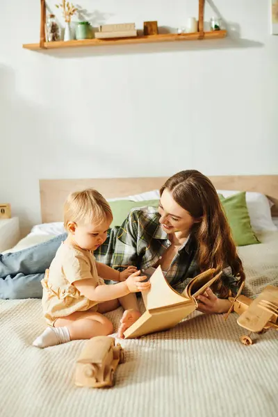 Eine junge Mutter und ihre kleine Tochter spielen mit Holzspielzeug auf einem gemütlichen Bett und schaffen gemeinsam gehegte Erinnerungen. — Stockfoto