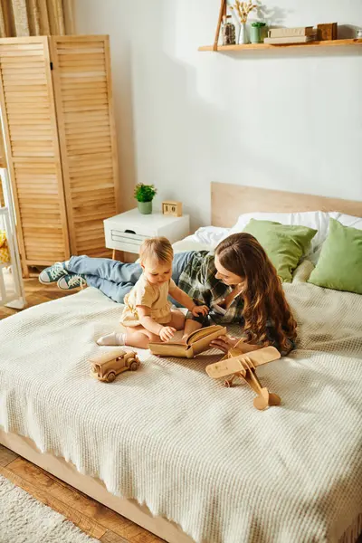 Une jeune mère lisant un livre à sa petite fille sur un lit douillet, créant un moment spécial de collage plein d'émerveillement et d'imagination. — Photo de stock