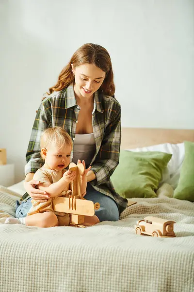 Une jeune mère joue joyeusement avec sa fille tout-petit sur un lit confortable, créant des souvenirs chaleureux ensemble. — Photo de stock