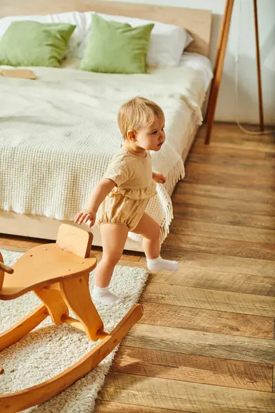 Uma criança jovem brinca alegremente com um brinquedo de baloiço de madeira, em um ambiente acolhedor em casa. — Fotografia de Stock