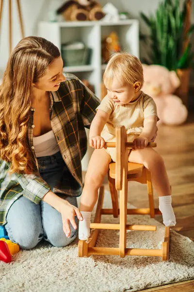 A young mother lovingly interacts with her baby daughter seated in a high chair, creating a heartwarming moment. — Stock Photo