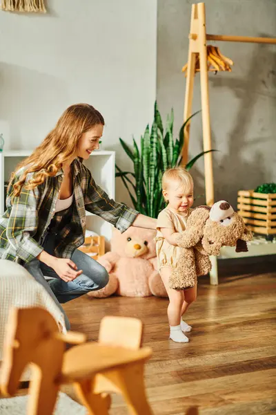 A young mother laughing as she plays with her baby girl and a teddy bear on the floor at home. — Stock Photo