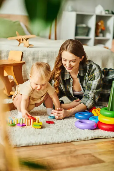 Una giovane madre interagisce felicemente con la sua bambina sul pavimento, impegnandosi nel gioco e creando momenti speciali insieme.. — Foto stock