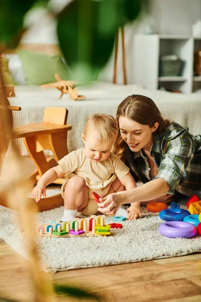 Una giovane madre si impegna gioiosamente con la sua bambina sul pavimento, favorendo un forte legame attraverso il gioco e l'interazione.. — Foto stock