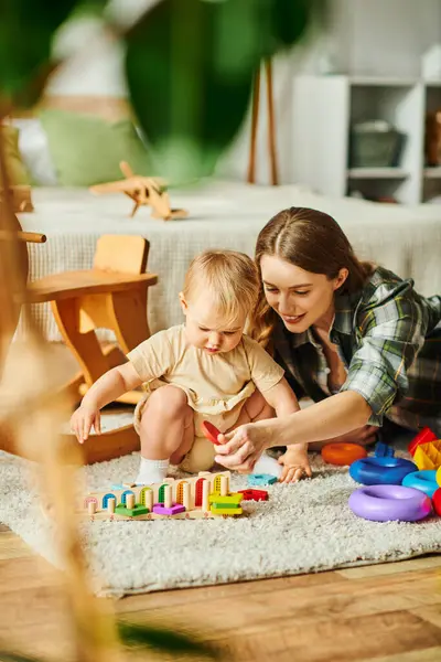 A young mother joyfully engages with her toddler daughter on the floor, fostering a strong bond through play and interaction. — Stock Photo