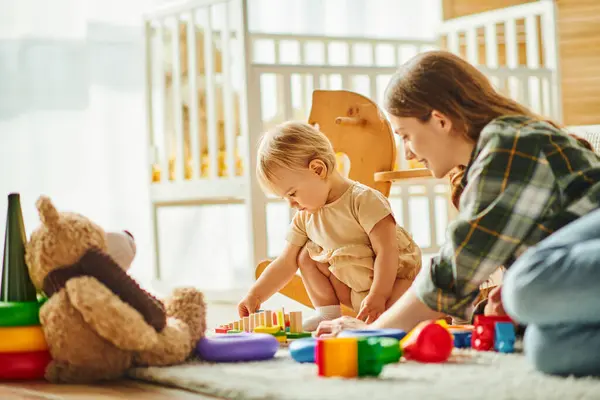 Una giovane madre e sua figlia minore si impegnano allegramente con i giocattoli sul pavimento, costruendo una forte e amorevole connessione.. — Foto stock