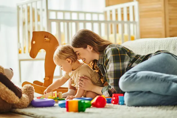 Una joven madre interactúa alegremente con su hija pequeña en el suelo en casa, creando valiosos recuerdos juntos. - foto de stock