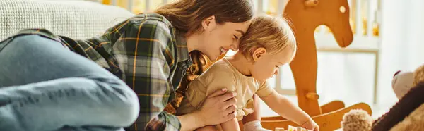 A young mother tenderly holds her toddler daughter in her arms, showing love and care in a cozy home setting. — Stock Photo