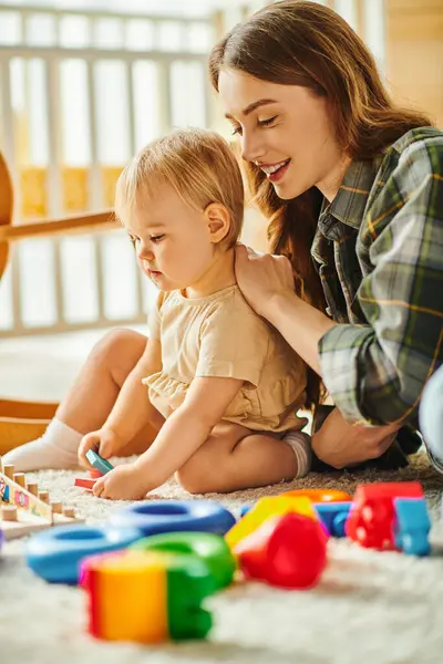 A young mother happily engages with her toddler daughter on the floor, sharing love and laughter in a tender moment. — Stock Photo