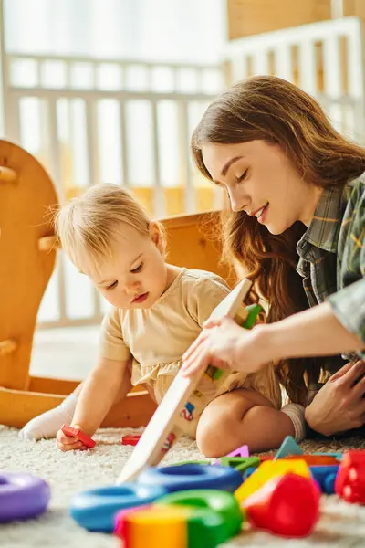 Una madre joven y su hija pequeña disfrutan de tiempo de calidad juntos, jugando con juguetes en el suelo en un ambiente acogedor en casa. - foto de stock
