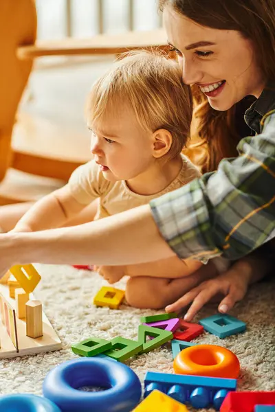 Uma jovem mãe e sua filha estão brincando alegremente com brinquedos no chão em casa. — Fotografia de Stock