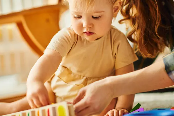 A young mother and her toddler daughter happily playing together, building structures with colorful blocks. — Stock Photo
