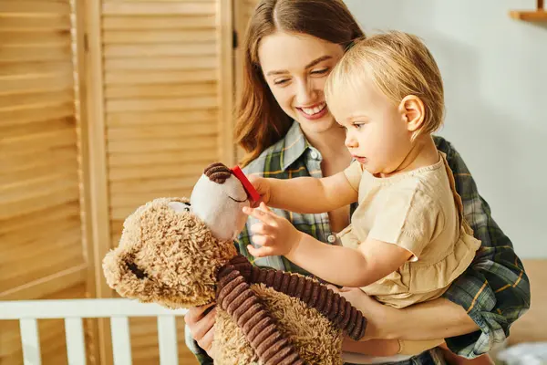 A young mother tenderly holds her baby daughter in one arm while a teddy bear sits in the other, creating a scene of love and comfort. — Stock Photo
