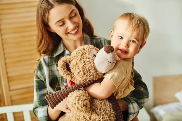 Une jeune mère tenant sa petite fille dans ses bras pendant que le tout-petit câline un ours en peluche, montrant amour et lien. — Photo de stock