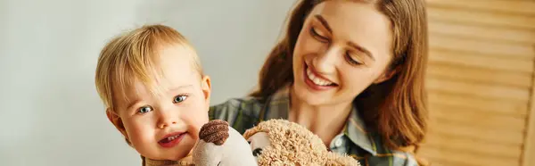 A young mother holds a teddy bear, smiling at her toddler daughter in a heartwarming moment of love and connection. — Stock Photo