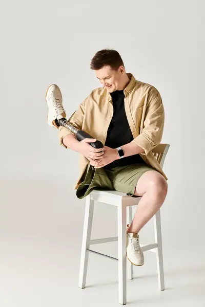 Un hombre guapo con una pierna protésica sentado en un taburete. - foto de stock