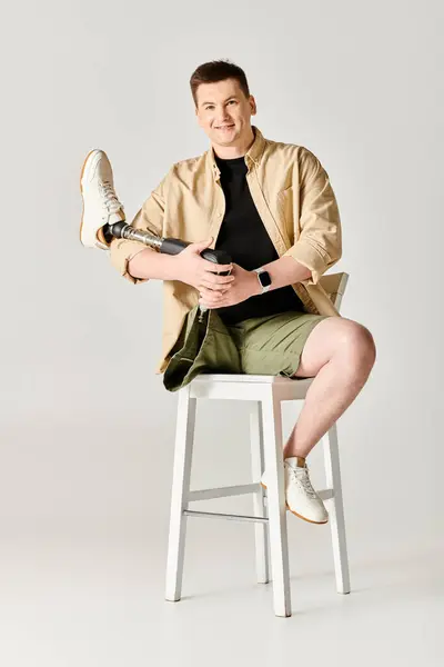 Ein gutaussehender Mann mit Beinprothese sitzt selbstbewusst auf einem weißen Hocker. — Stockfoto
