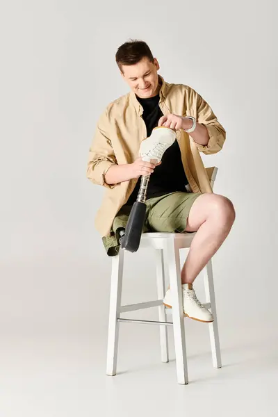 Hombre atractivo con una pierna protésica sentada en un taburete. - foto de stock