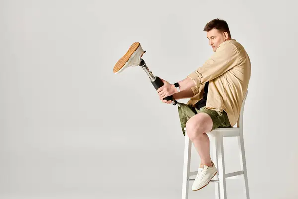 Un hombre guapo con una pierna protésica se sienta con confianza sobre un taburete blanco. - foto de stock