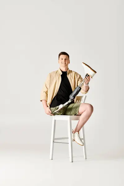 Un hombre guapo con una pierna protésica se sienta confiadamente encima de una silla blanca. - foto de stock