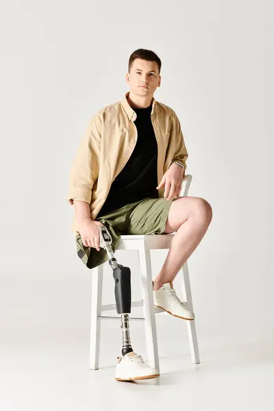 Schöner Mann mit Beinprothese posiert aktiv auf weißem Stuhl. — Stockfoto