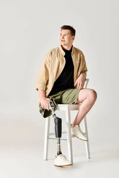 Красивий чоловік з протезною ногою сидить на білому табуреті. — стокове фото