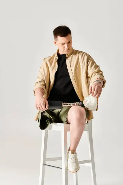 A handsome man with a prosthetic leg confidently sits atop a white stool. — Stock Photo